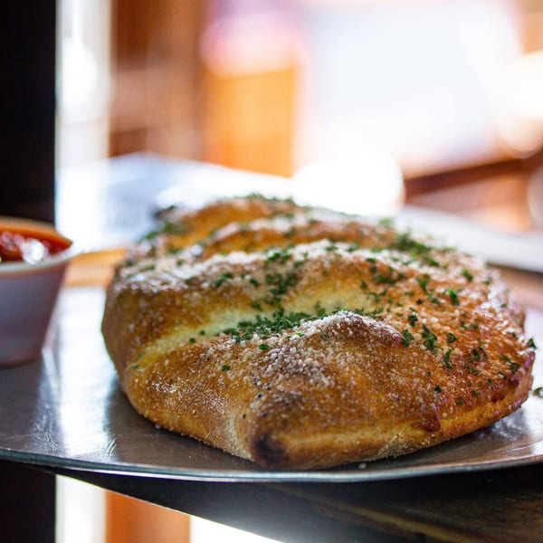 Golden brown NYP Slice House calzone, topped with parmesan and parsley, on a metal pizza tray.
