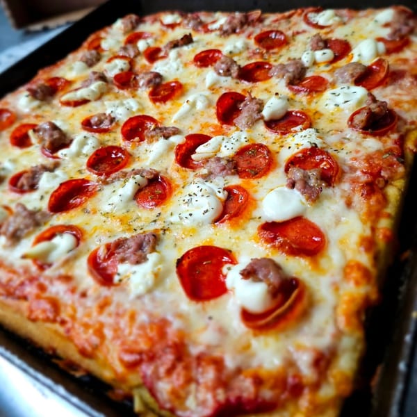 Close-up of a square NYP Slice House pizza with pepperoni, sausage, and ricotta cheese.