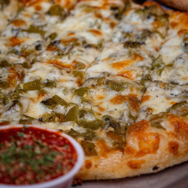 A close-up of a NYP Slice House pizza with green peppers and melted cheese, with a side of red sauce.