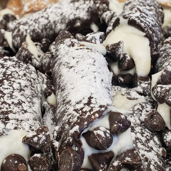 Chocolate cannolis filled with white cream and chocolate chips, dusted with powdered sugar.