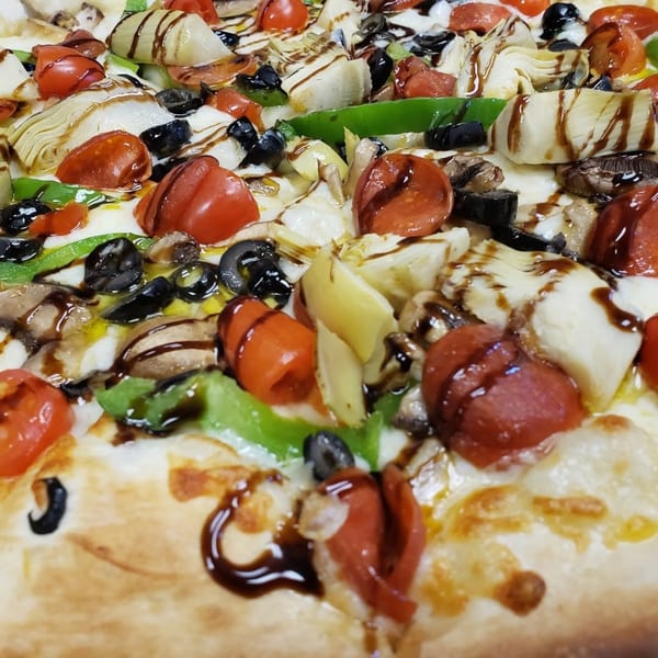 Close-up of a NYP Slice House pizza with tomatoes, olives, artichokes, mushrooms, and balsamic glaze.