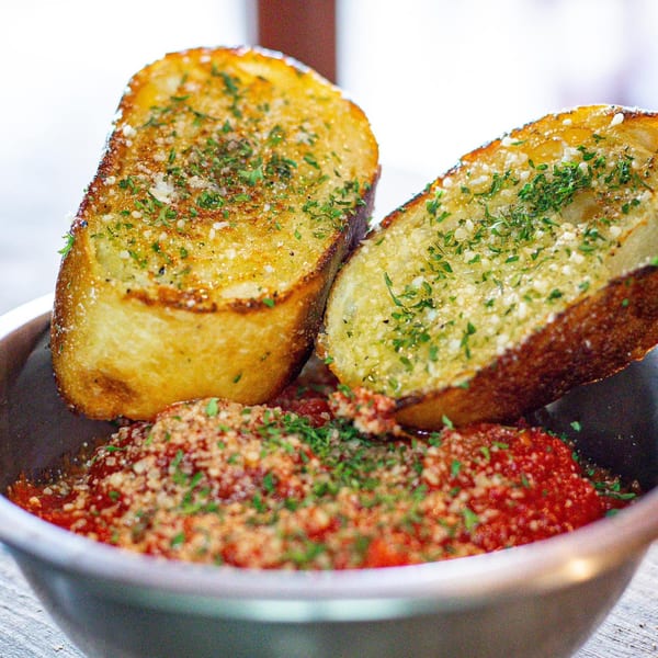 Two pieces of garlic bread with parsley and parmesan cheese in a bowl of marinara sauce.