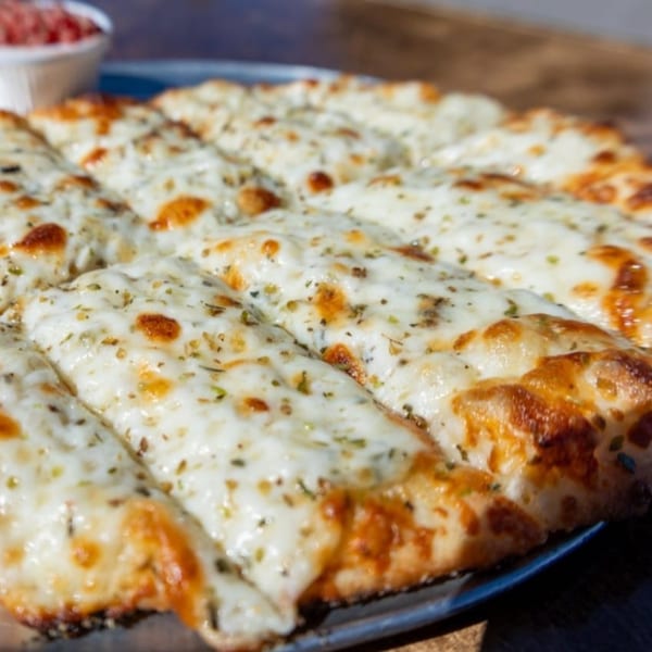 NYP Slice House Pizza's cheesy garlic breadsticks, golden brown with herbs, served with marinara.